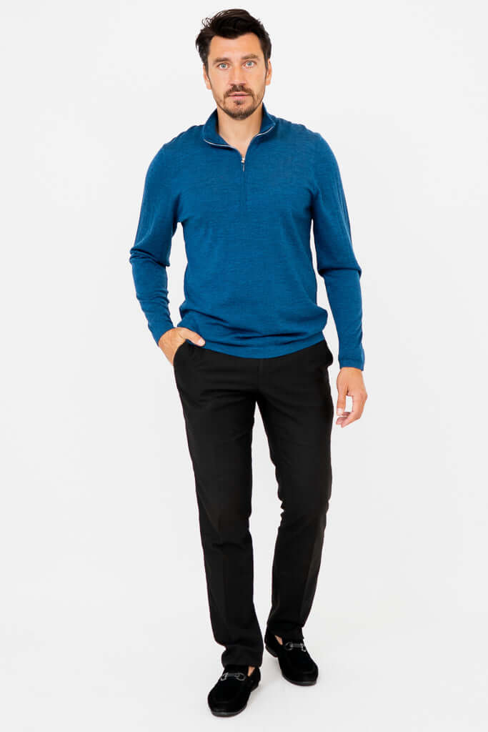 Man standing with hands in pockets in a blue merino sweater and black pants