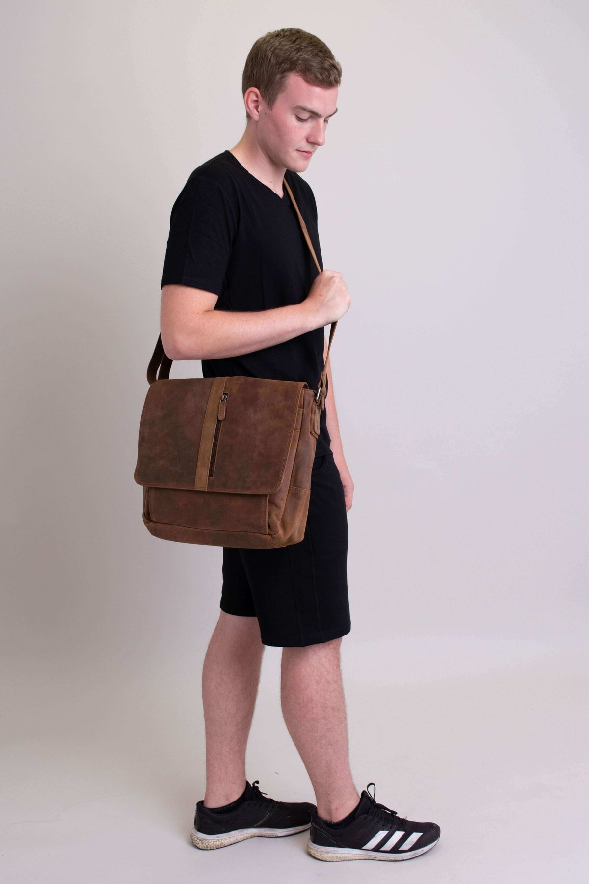 Man looking down carrying brown buffalo leather messenger bag, adjustable crossbody strap
