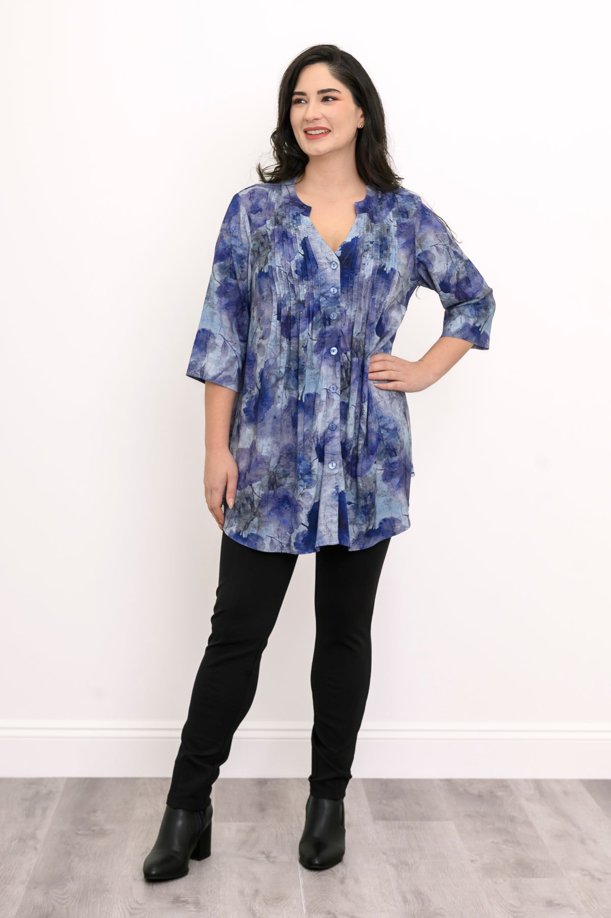Straight-on full body portrait of an elegant women's blue patterned 3/4 sleeve tunic shirt and black pants