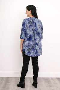 Back view of a loose-fit blue floral linen bamboo blend blouse with pin-tucks, black pants, and boots.