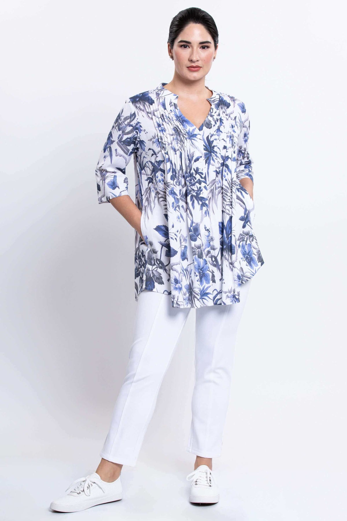 Woman showing side inseam pockets of Margate blue floral pin tuck blouse with white pants