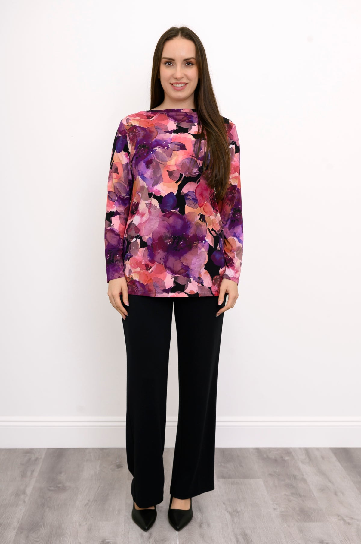 A-line pink floral print bamboo blouse with a boat neck, styled with black trousers against a white wall.