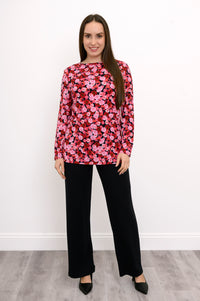 Model wearing a pink and red botanical print A-line tunic paired with black fitted trousers, standing front-facing.