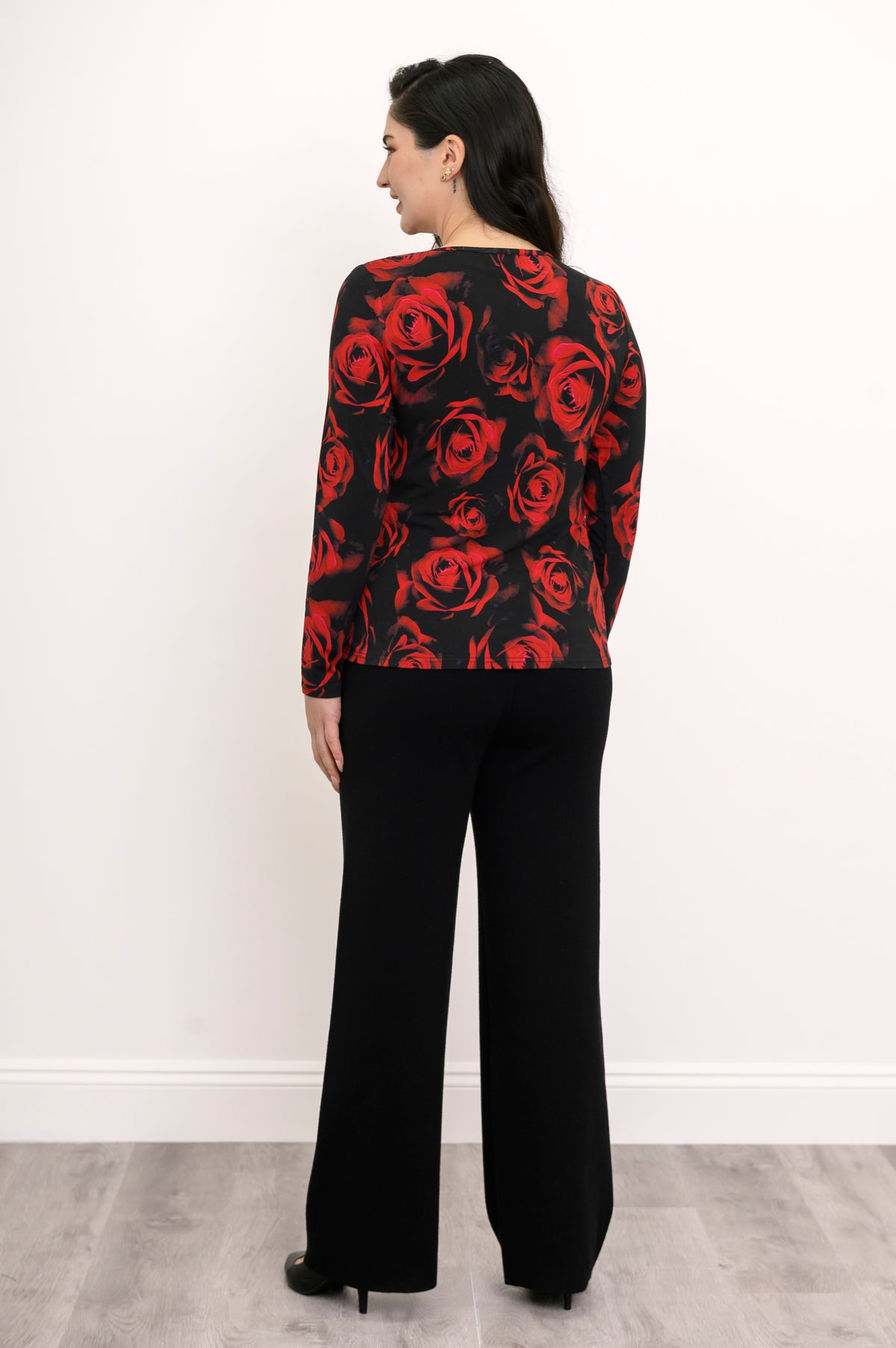 Back view of a women's round neck red floral print shirt, styled with dark trousers against a white background.