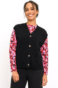 Smiling woman wearing an onyx button-up knit vest layered over a bright pink floral long-sleeve top, front view.