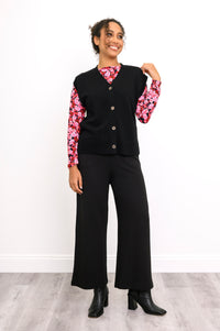Front-facing view of a button-down black sweater vest paired with a vibrant pink-red botanical print shirt.