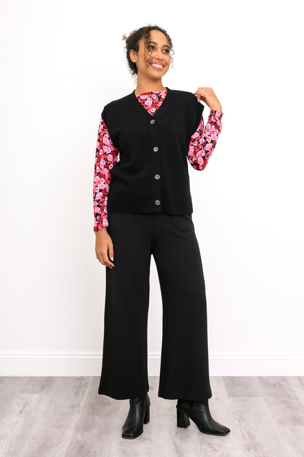 Front-facing view of a button-down black sweater vest paired with a vibrant pink-red botanical print shirt.