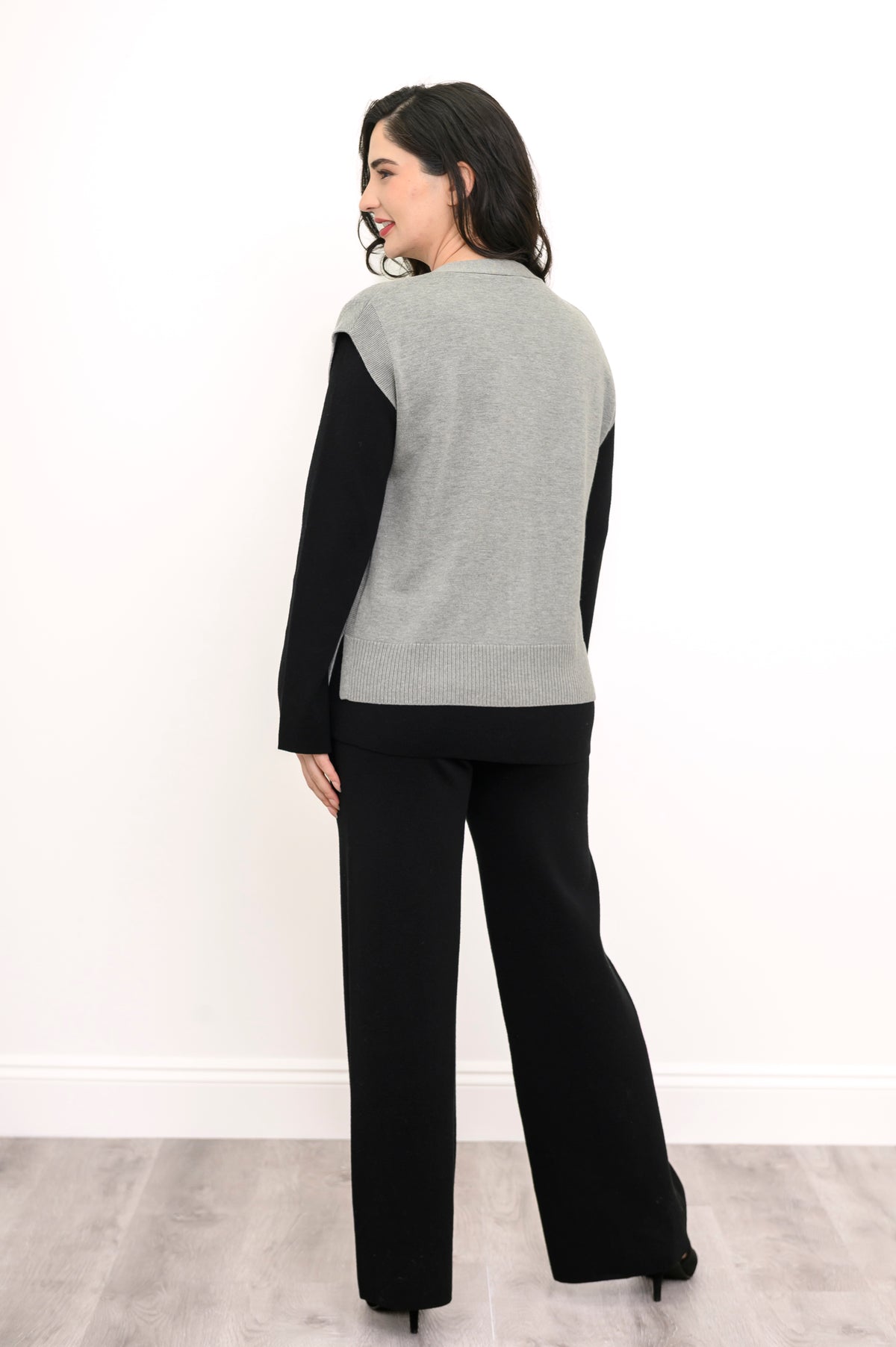 Back view of a light gray knit vest, highlighting the flattering extended shoulder cut and deep ribbed waist.