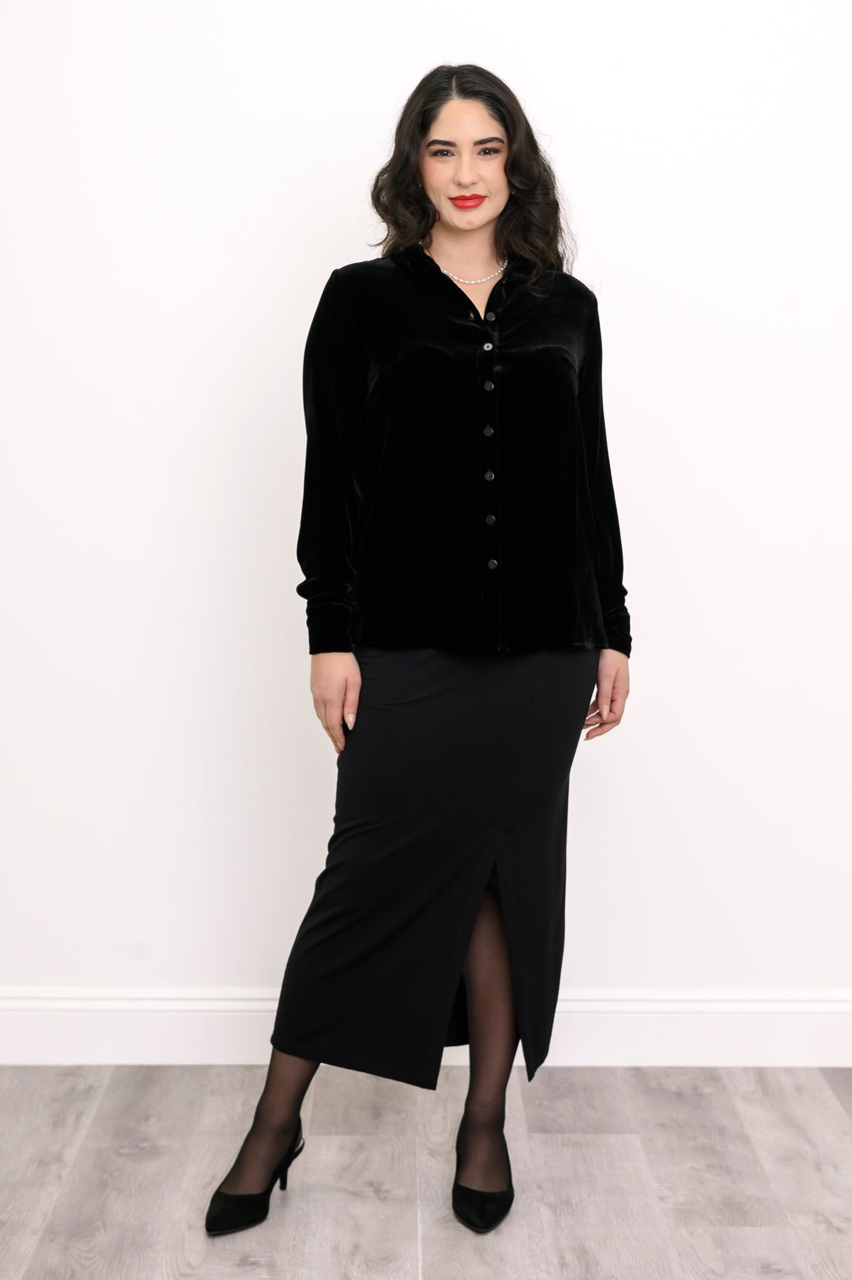 Full-length front view of a woman wearing a black silk velvet button-up shirt and a matching front-slit maxi skirt