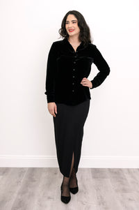 Wide studio shot of an elegant women's black velvet long-sleeve blouse paired with a long black skirt and heels