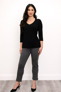 Full body view of woman with her hands at her side wearing a black top and grey slim fit pants