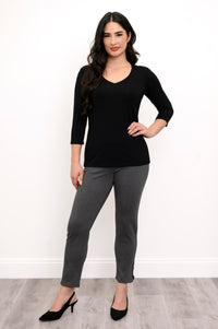 Woman posing with her hand on her hip while wearing a black v-neck shirt, grey pants, and black pumps