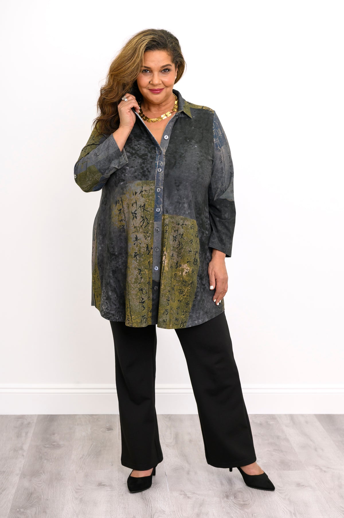 Button-down long-sleeve green knit tunic featuring shirt-style collar, styled with dark pants.