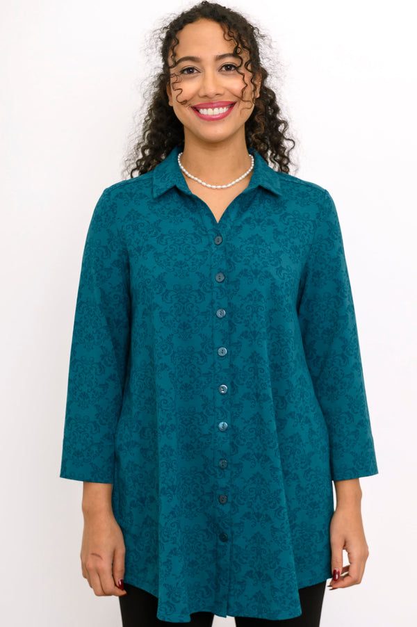 Smiling woman wearing a teal damask pattern button-up bamboo tunic with a classic collar and three-quarter sleeves.