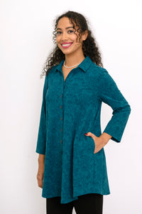 Women's flowy teal geometric print bamboo-cotton blouse featuring a collar and buttons, styled against a white wall.