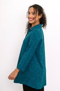 Smiling woman looking over her shoulder in a teal patterned bamboo shirt-jacket with 3/4 sleeves, side view.