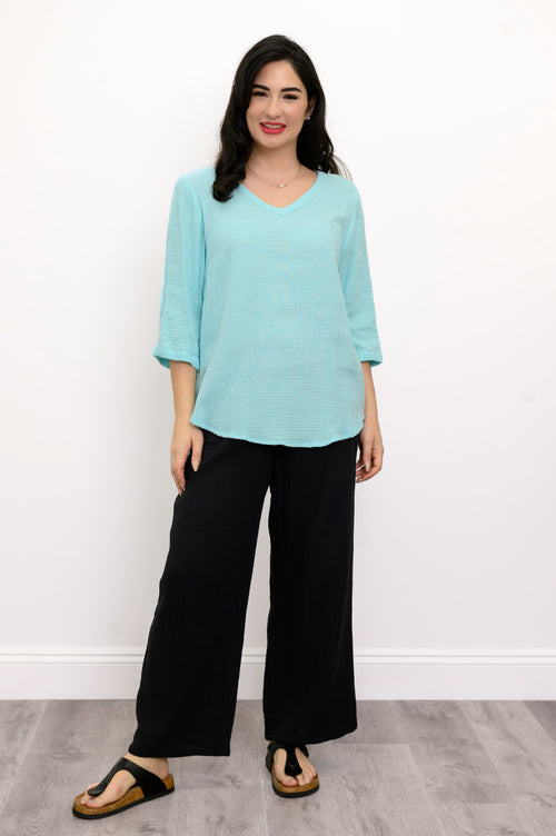 Woman wearing a light blue top, black pants, and black sandals against a white background, front view