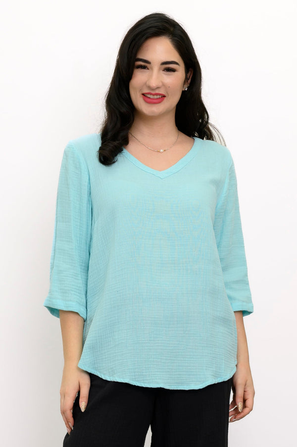 Woman wearing a light blue top, black pants, and black sandals against a white background, front view