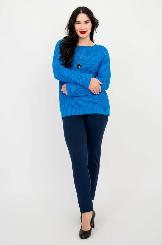 Model crossing arms, wearing blue hip-length sweater with navy pants and black heels