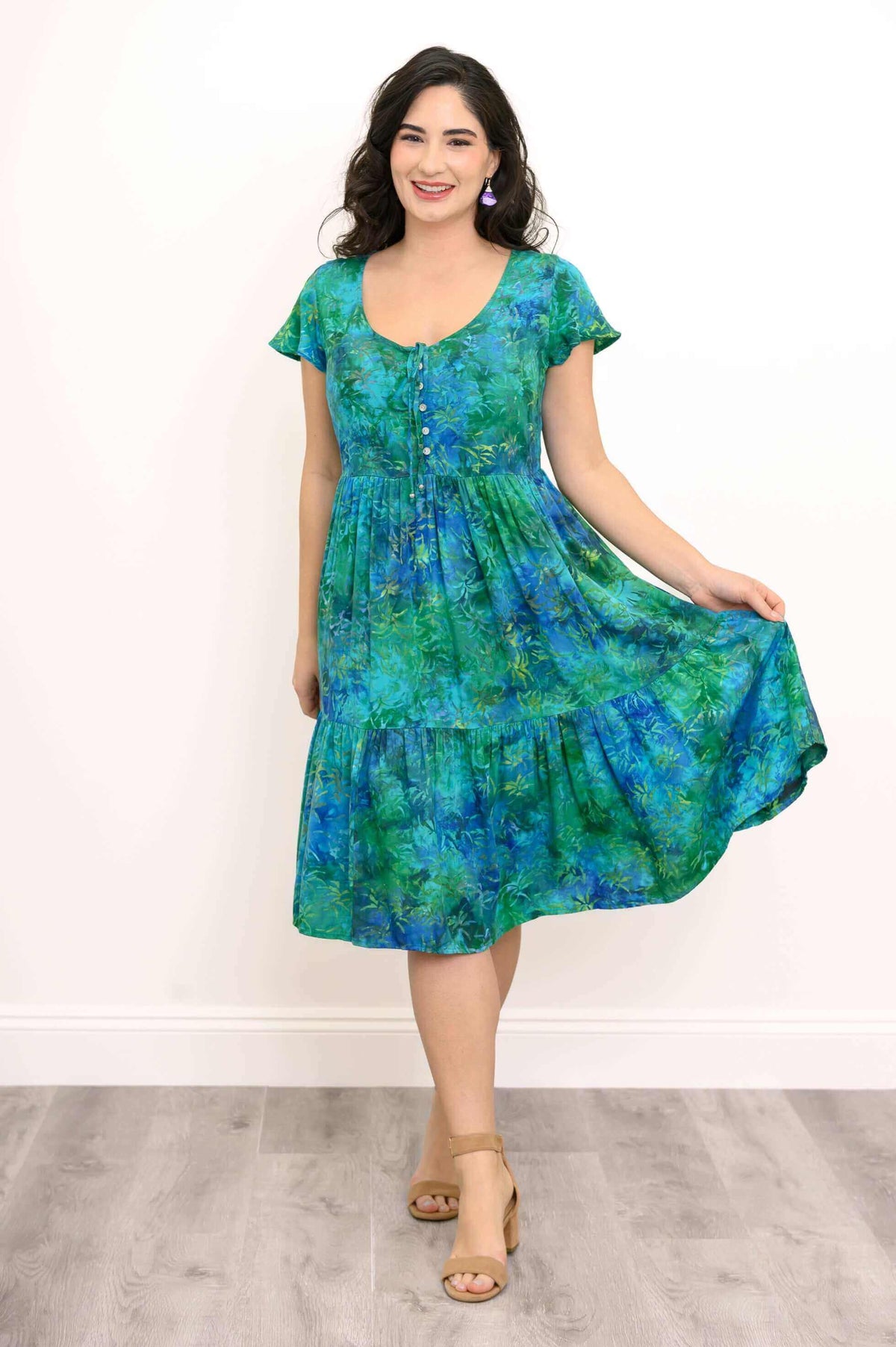 Woman holding out skirt of green and blue tiered midi dress, smiling