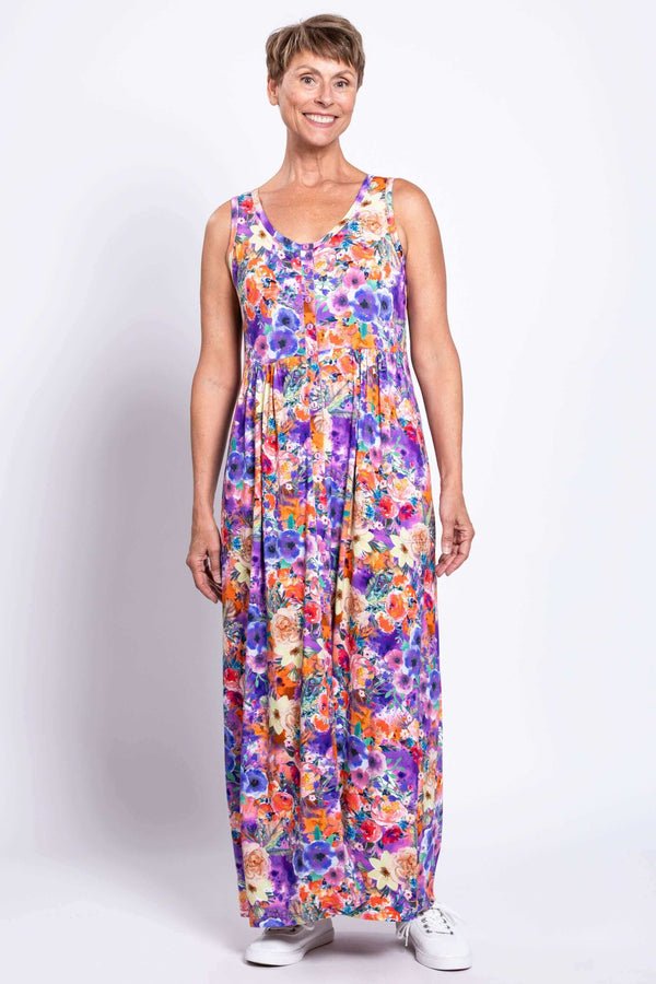 Woman in a vibrant floral sleeveless maxi dress, standing facing front with hand at side