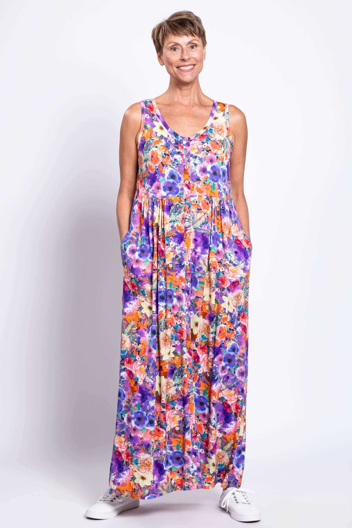 Woman wearing a sleeveless maxi dress with a colorful floral pattern and pockets, facing front