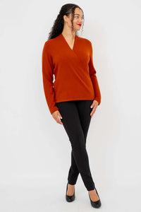 Woman modeling rust cashmere surplice sweater with crossed legs