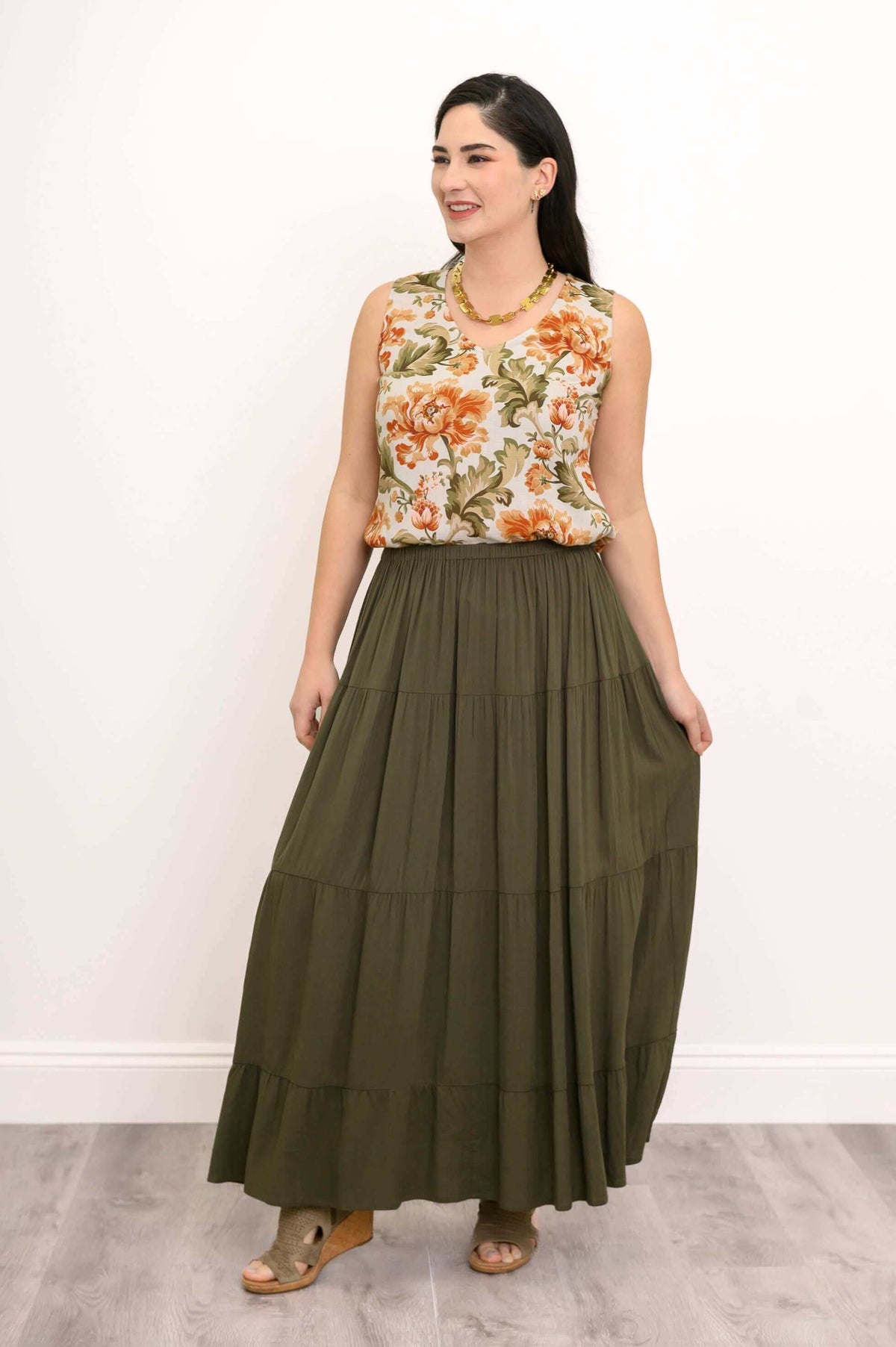 Model smiling and holding olive green tiered maxi skirt, floral blouse visible