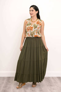 Model smiling and holding olive green tiered maxi skirt, floral blouse visible