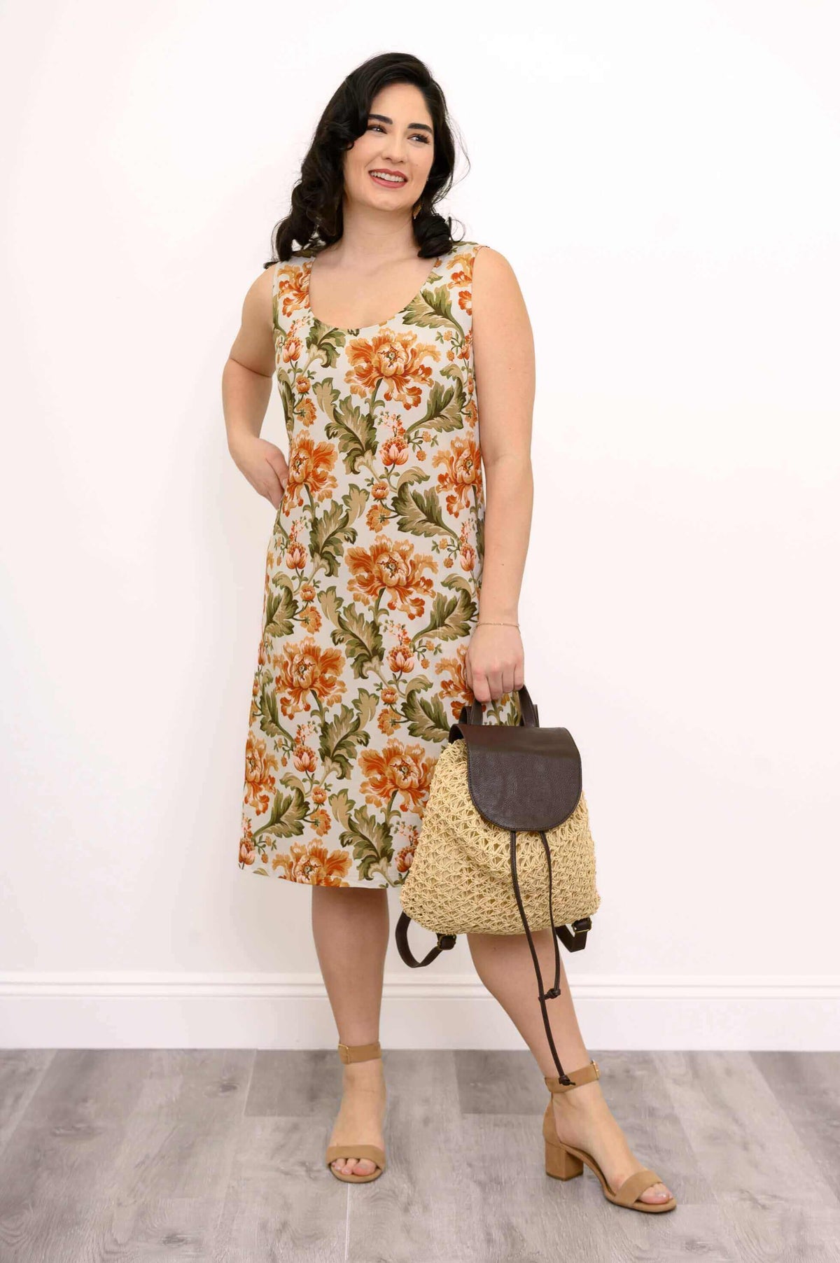 Model posing with floral dress and woven bag, hand in pocket
