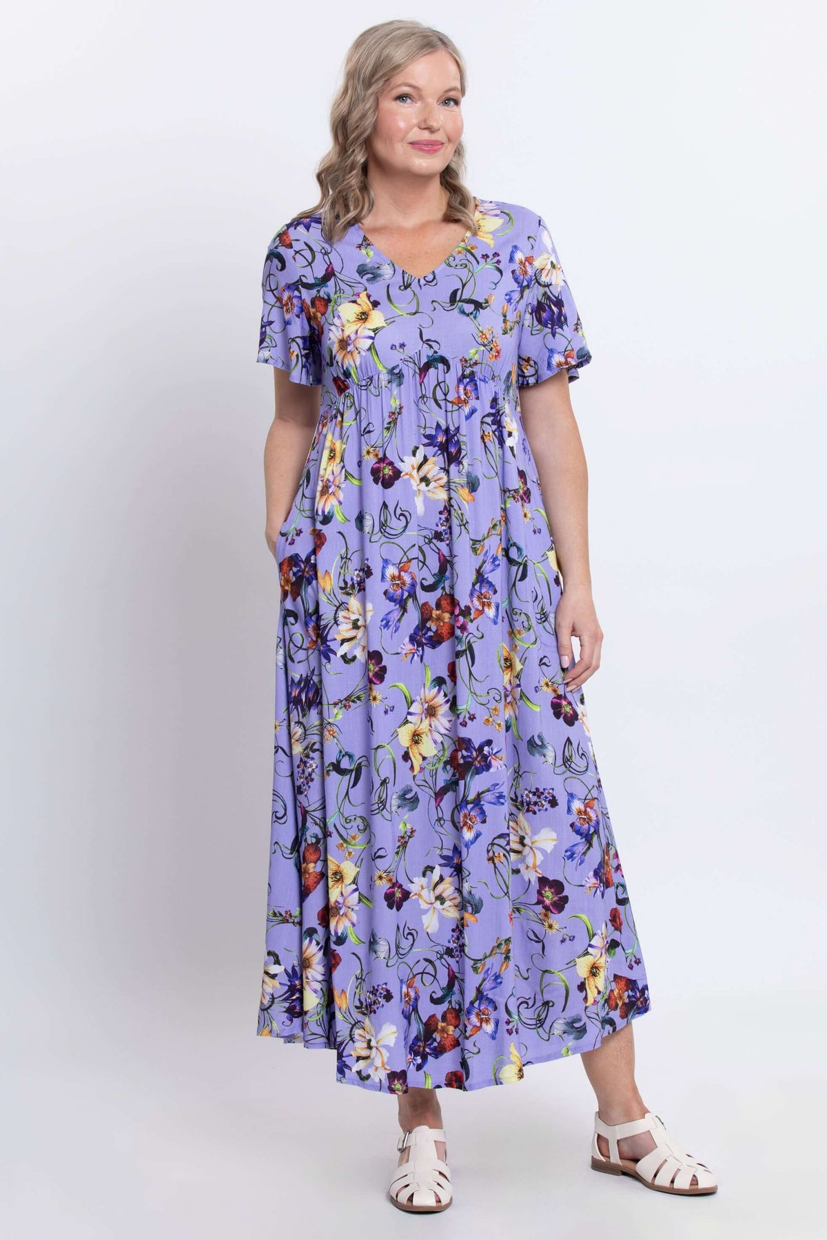 Woman posing in a lavender floral empire waist maxi dress with hands in pockets