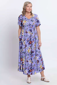 Woman posing in a lavender floral empire waist maxi dress with hands in pockets