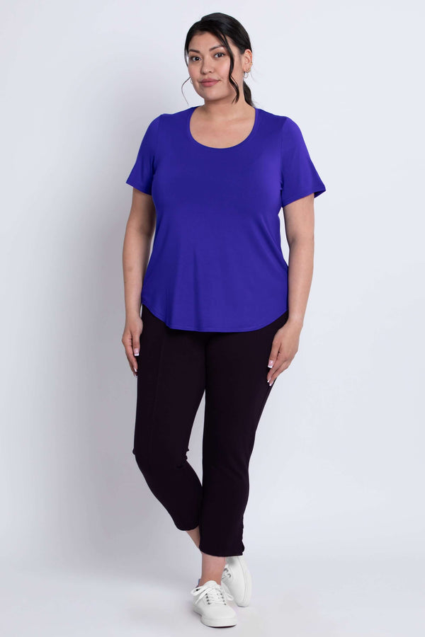 Woman standing in a purple scoop neck tee and dark cropped pants, front angle