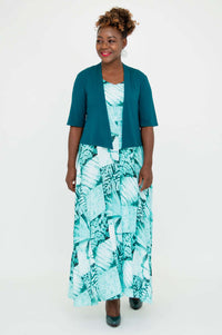 Model smiling in teal bamboo cropped jacket and long blue geometric dress, front view