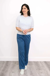 Model in a white cardigan and blue pants standing with hands clasped