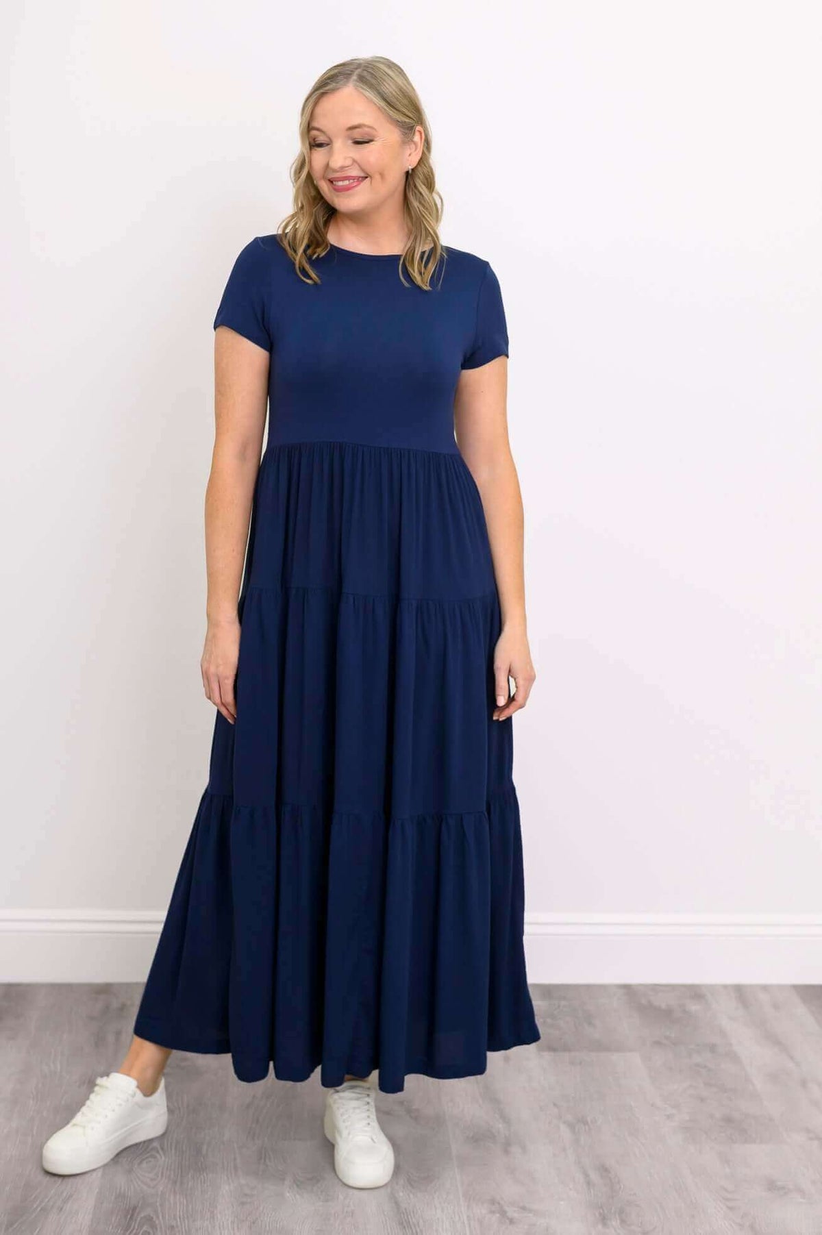 Woman in navy blue empire waist maxi dress, looking down and smiling