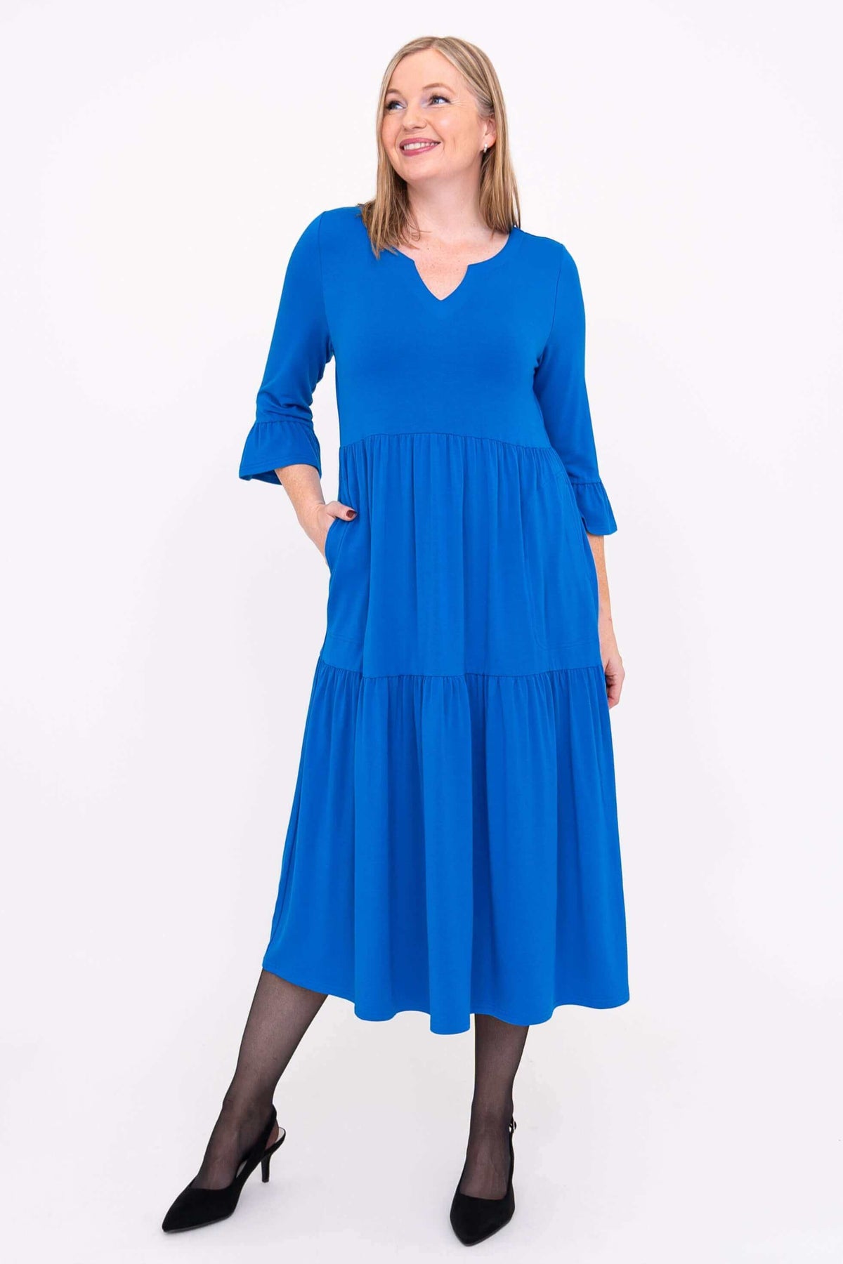 Model looking up in blue tiered midi dress with pockets and ruffle sleeves, front view