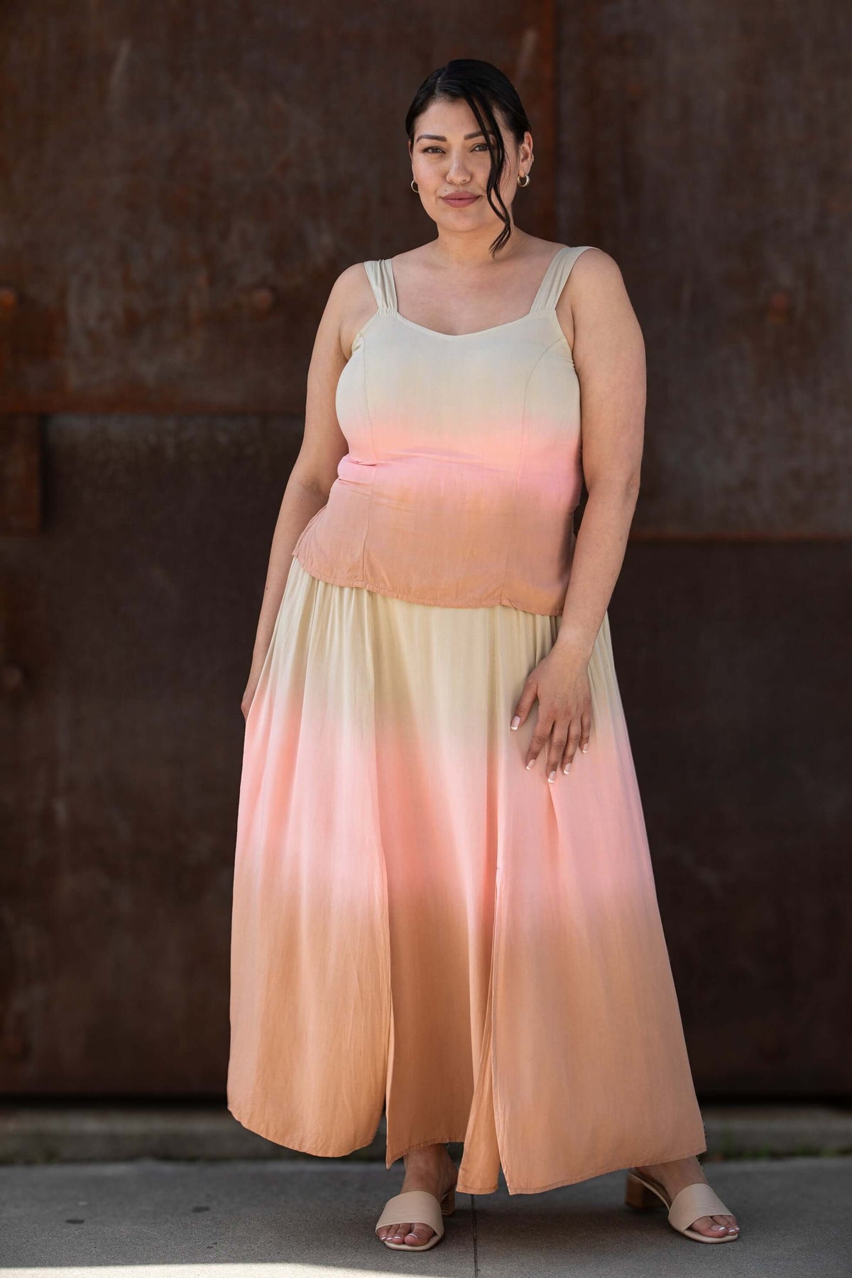 Woman in a sleeveless ombre maxi dress standing outdoors against a textured wall