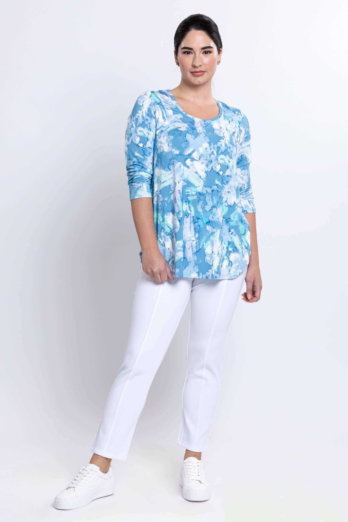 Model posing in blue watercolor top and white pants, angled stance