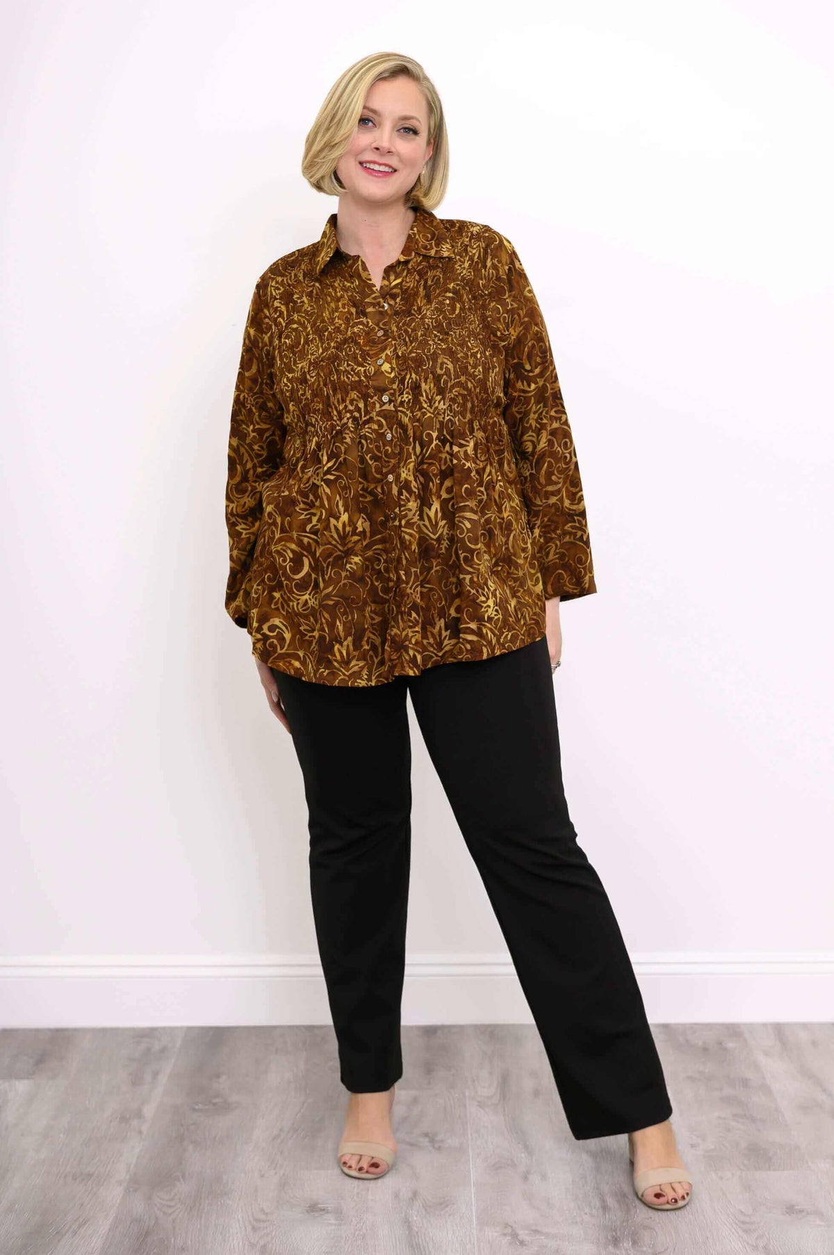 Model in brown floral smocked shirt with black pants, posing with hand on hip