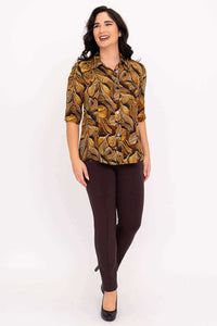 Model in golden leaf print blouse and brown pants, smiling and posing