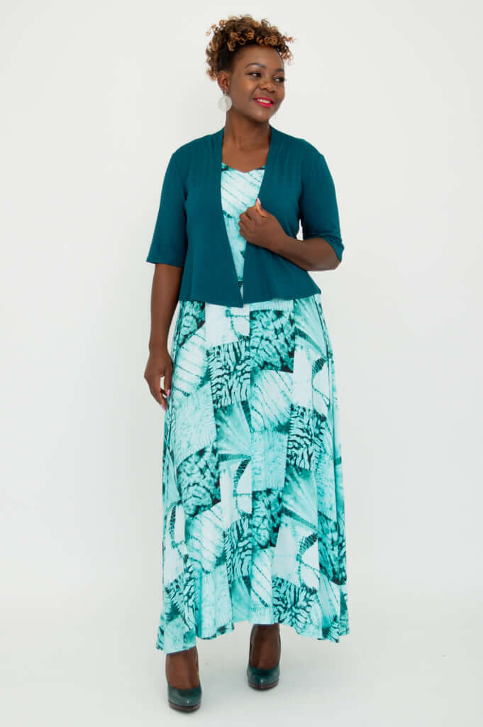 Model posing with hand on jacket, wearing teal cropped jacket and patterned dress