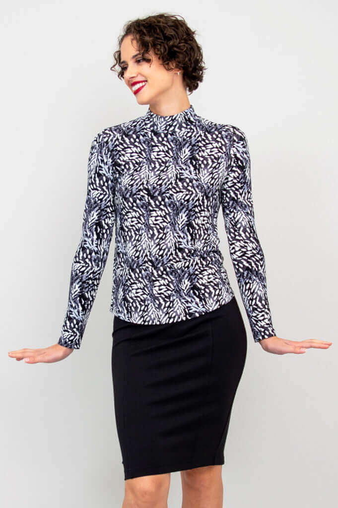 Woman in black and white palm mock neck top smiling and posing playfully, hands out