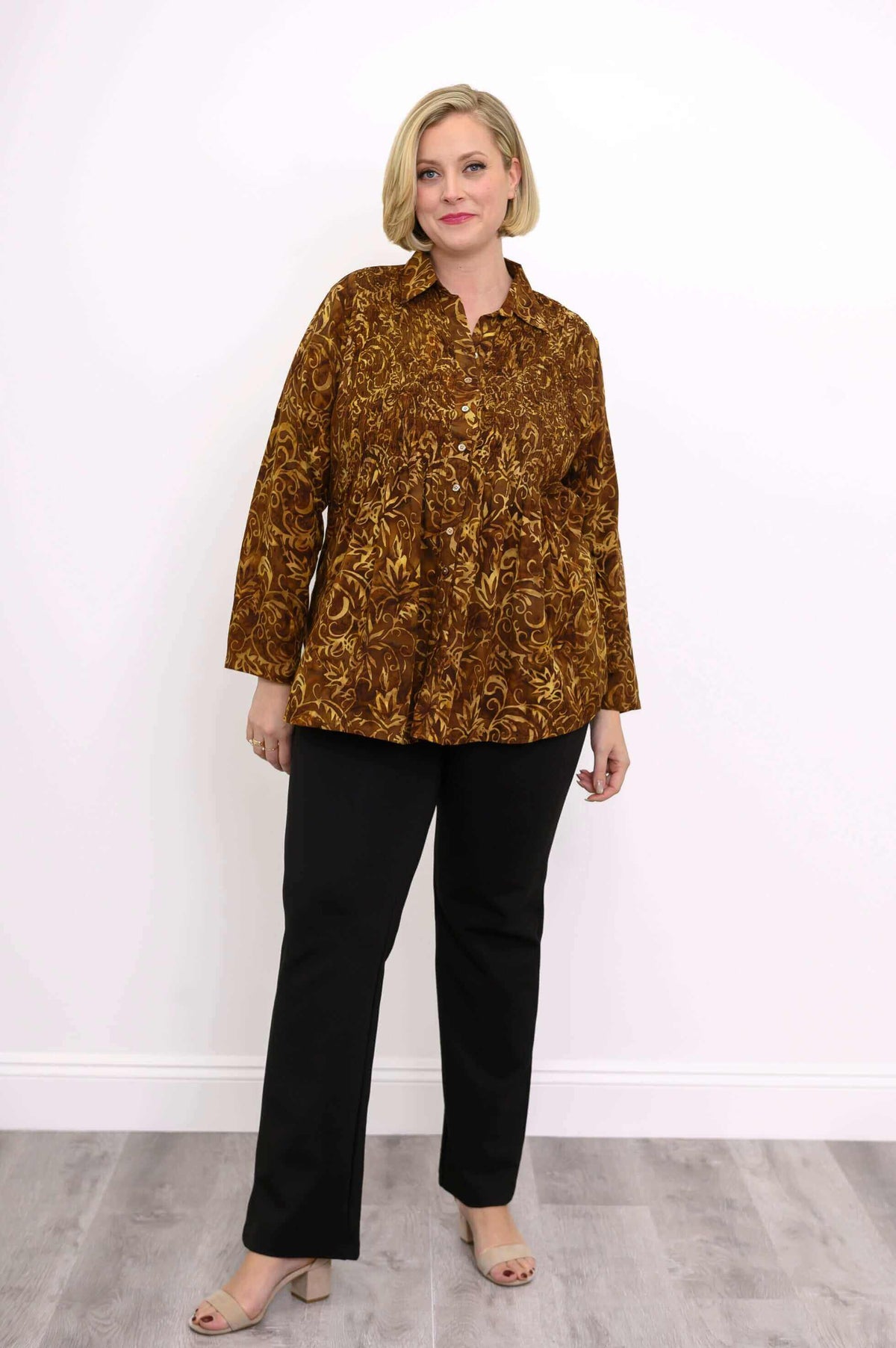 Model in brown floral smocked shirt and black pants, standing against a white background