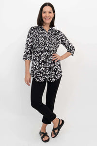 Model posing front-on in black and white patterned 3/4 sleeve blouse and black pants