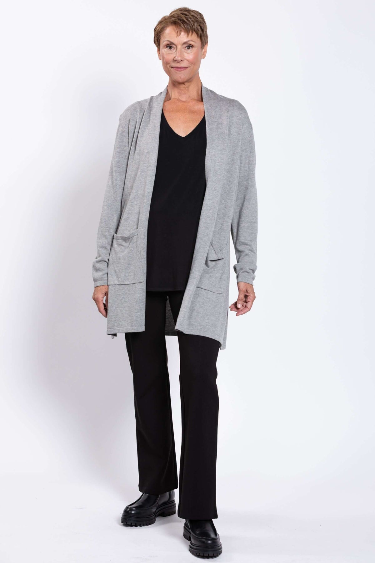 Model in long grey cardigan with patch pockets, standing against white background