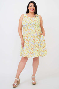 Woman in a sleeveless yellow floral dress with pockets and wedge sandals