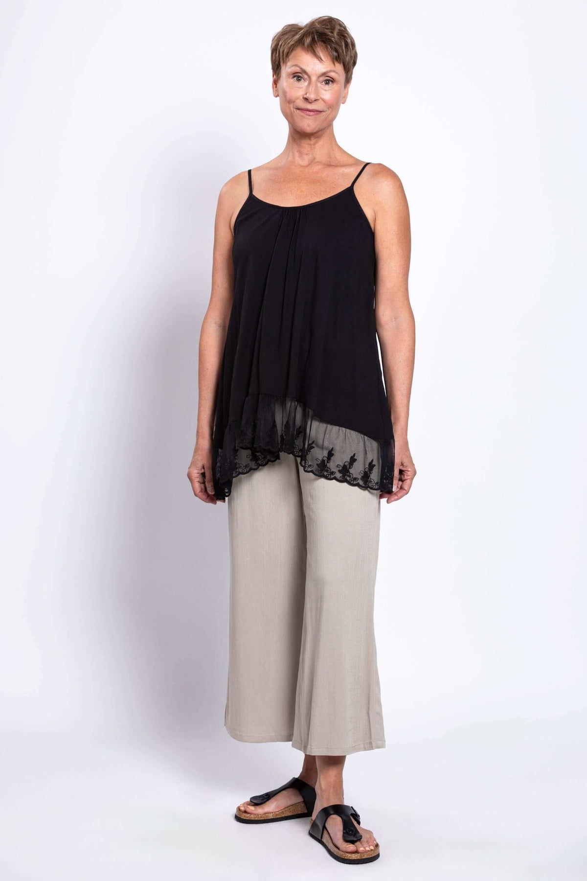 Woman modeling a black tank top with lace hem paired with beige wide-leg pants