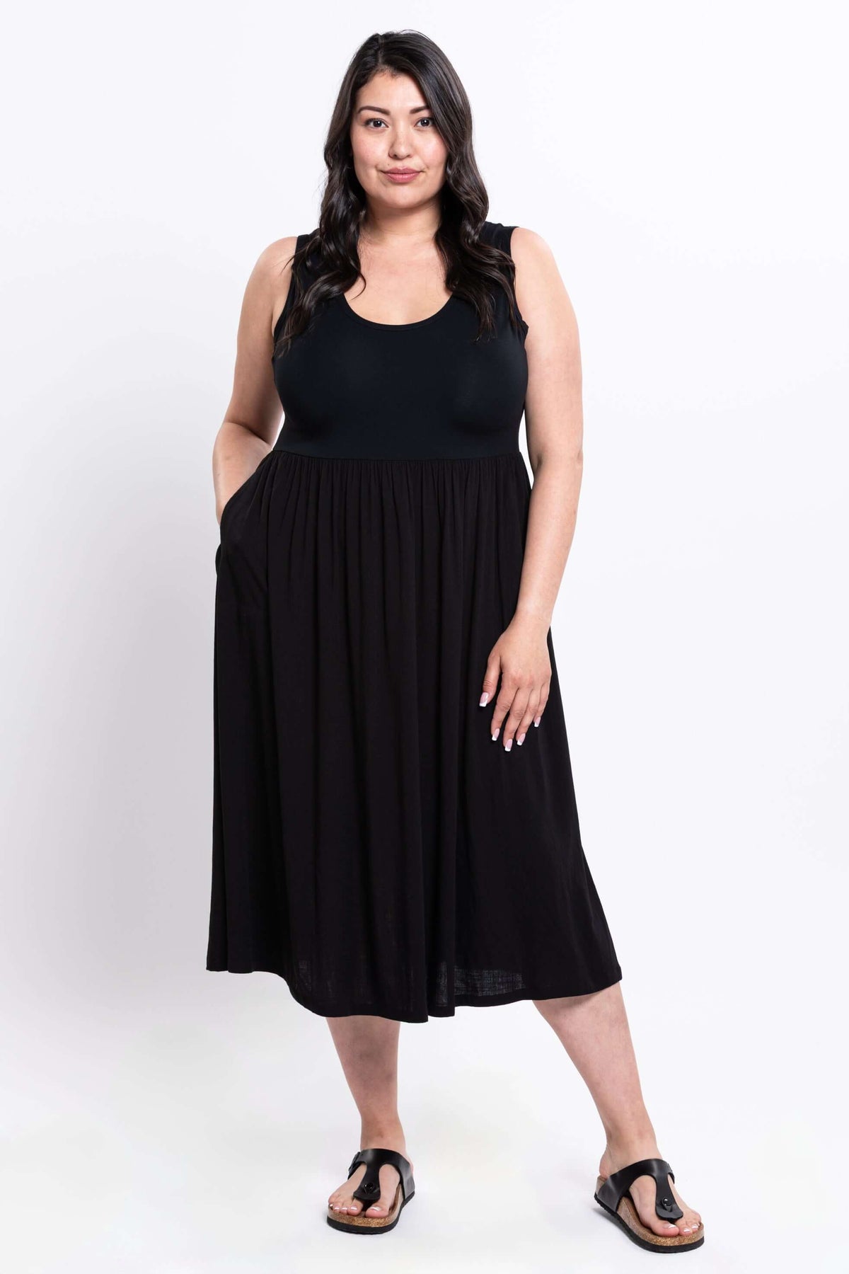Model wearing a black sleeveless empire waist midi dress with pockets and sandals