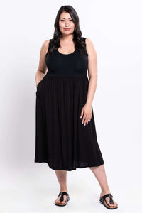 Model wearing a black sleeveless empire waist midi dress with pockets and sandals
